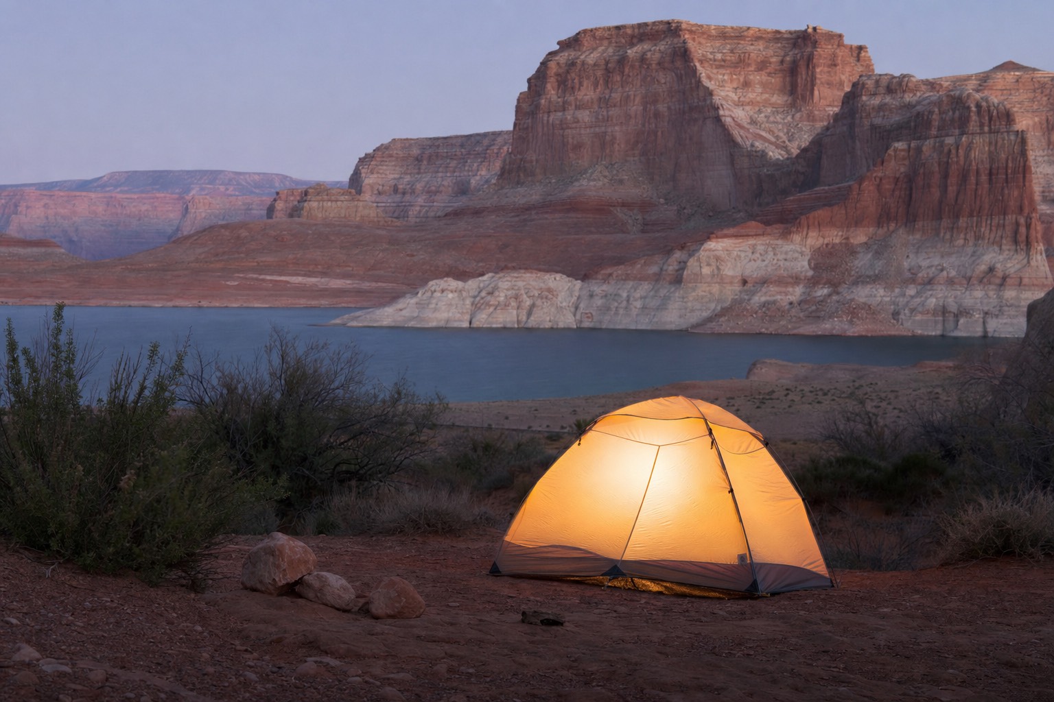 Tent glowing at dusk on a desert campsite near Lake Powell with sandstone cliffs behind