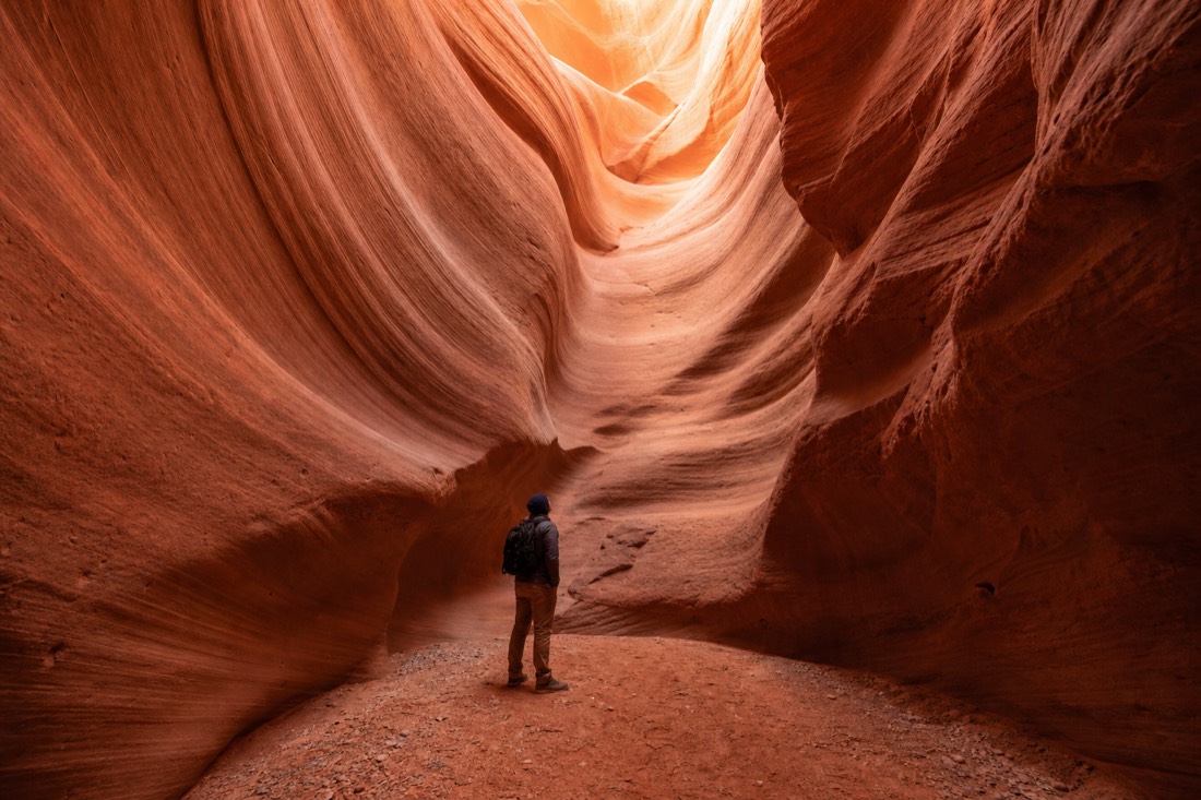 Lone visitor standing in a wide chamber of a slot canyon looking up at curved walls