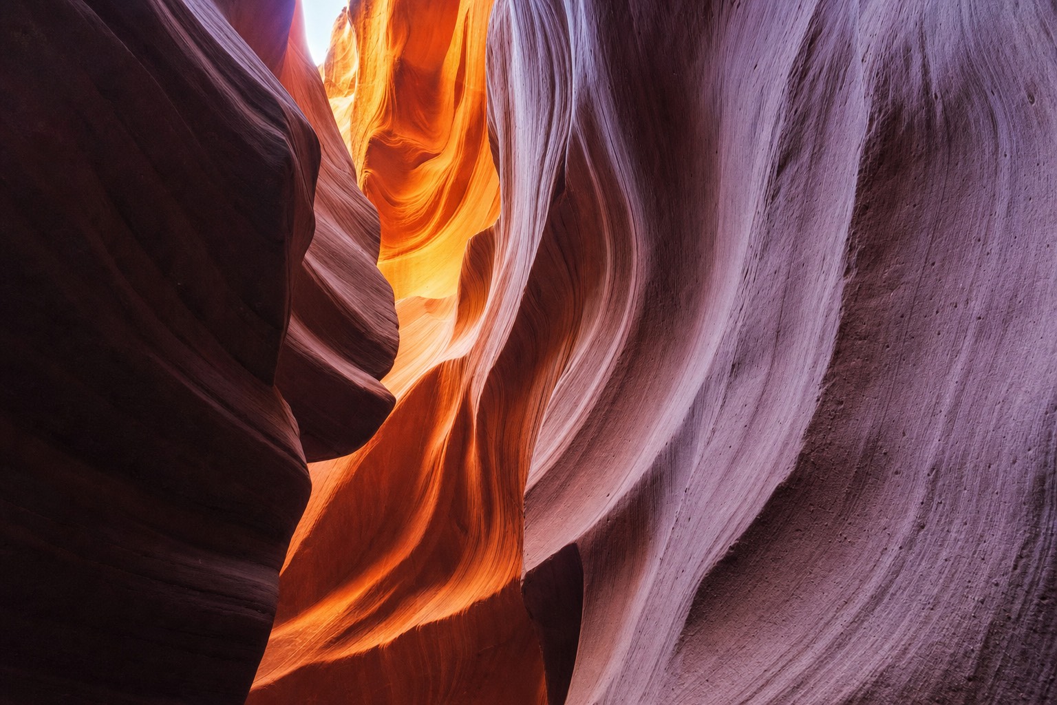 Sculpted sandstone slot canyon walls curving upward in glowing orange and violet light