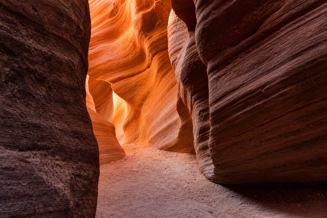 Morning light entering a quiet slot canyon with warm glow on layered sandstone walls