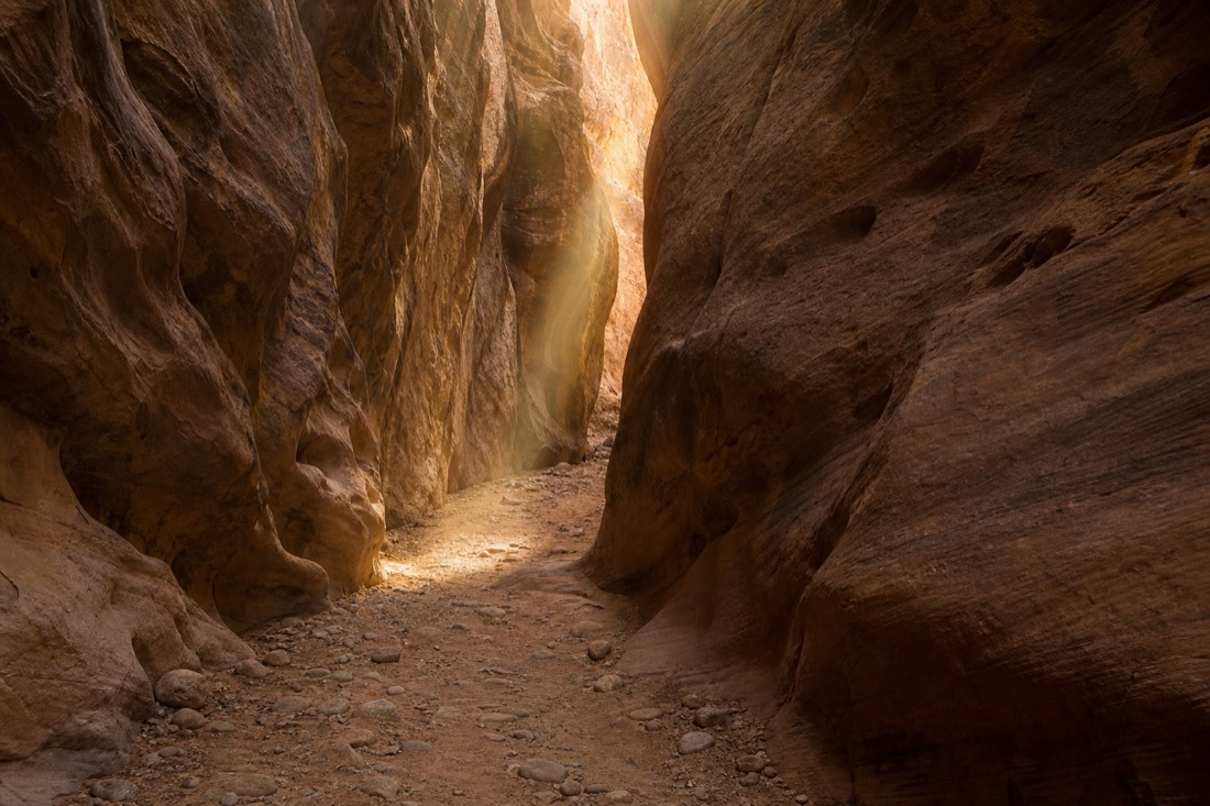 Morning light reaching down between smooth canyon walls onto an empty sandy path