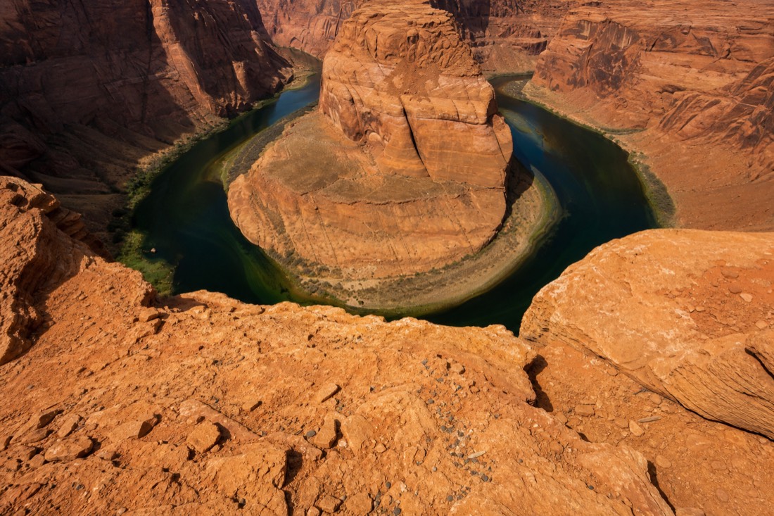Horseshoe-shaped river bend far below a sandstone rim viewpoint under strong sun
