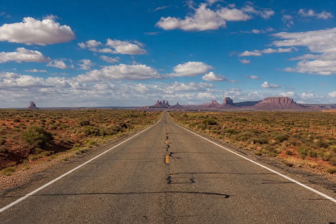 Long empty desert highway running toward distant buttes under a huge sky