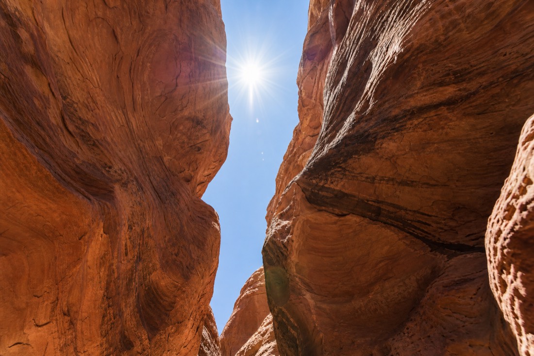 Diagram-style view upward through a slot canyon crack toward the midday sun directly overhead