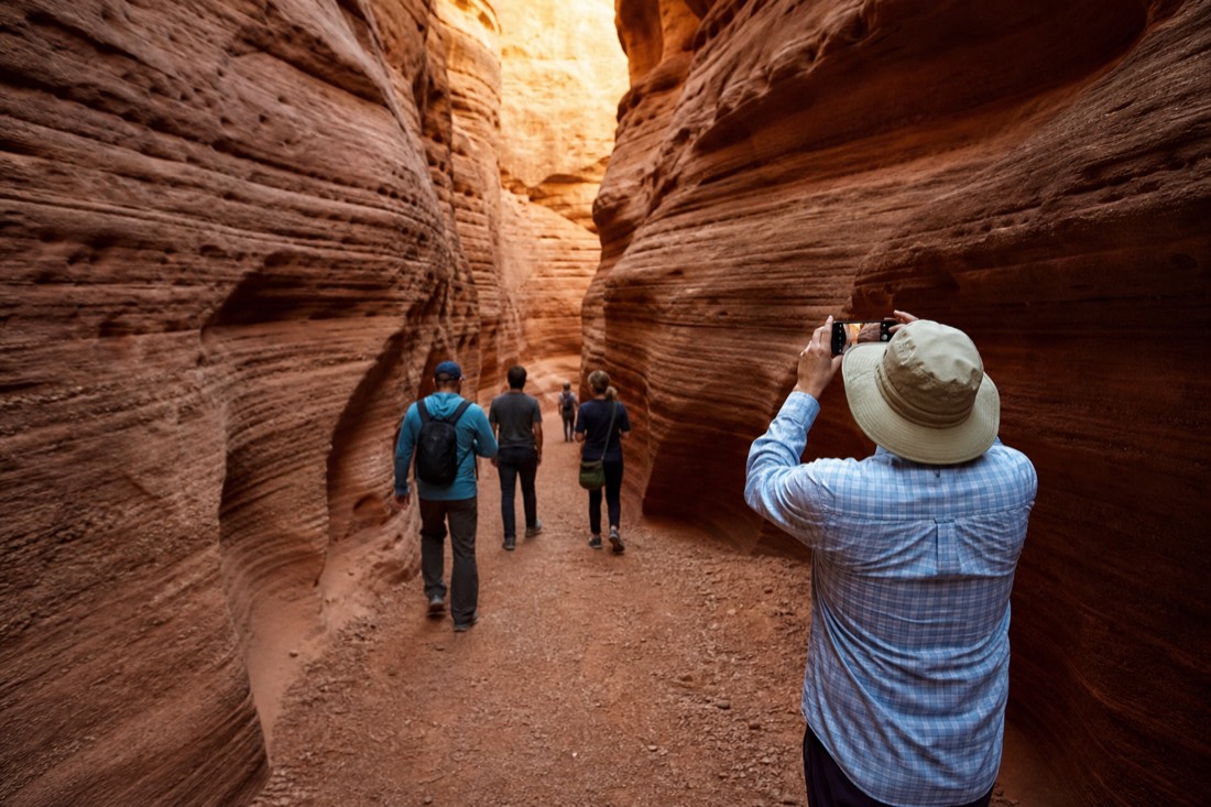 Guided group walking through a sandstone slot canyon carrying only phones and small cameras