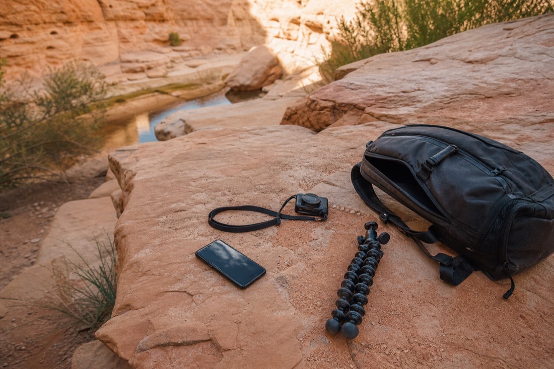 Flat lay of allowed canyon gear: phone and small camera on a strap, with tripod and backpack set aside