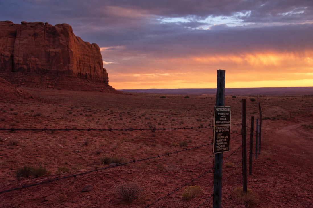 Fenced tribal park boundary in red rock desert with warning signage silhouetted at dusk