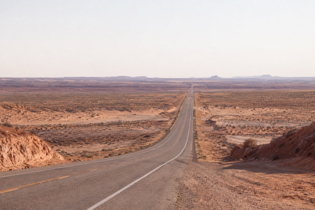 Empty desert highway crossing a sandy wash with no visible canyon opening in the flat terrain