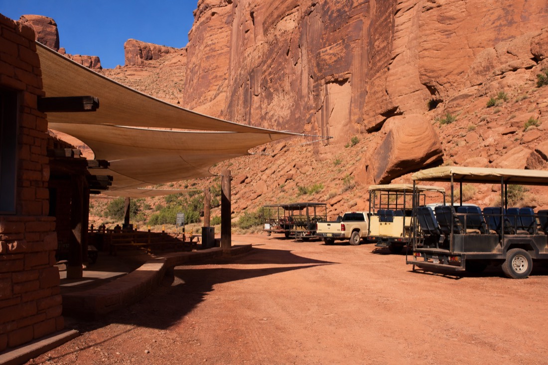 Shade canopies and tour vehicles at a desert check-in station with guides greeting arriving visitors