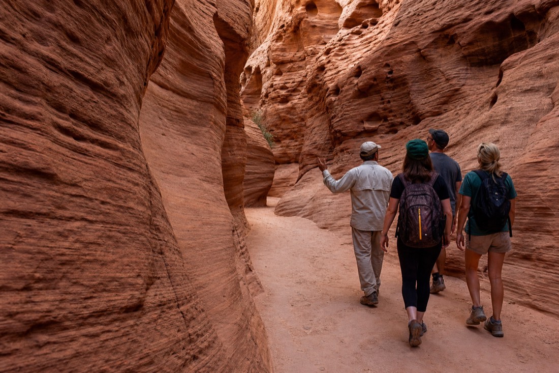 Small group of three visitors walking with a guide through an empty winding slot canyon passage