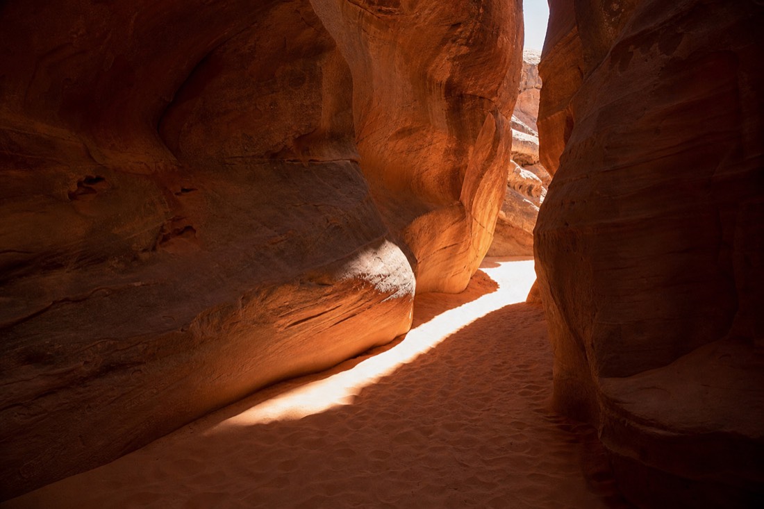 Bright midday sunbeam cutting through a slot canyon opening onto rippled sand