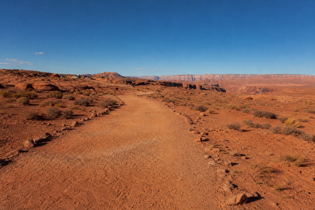 Wide desert trail leading from a parking area toward the Horseshoe Bend rim under open sky