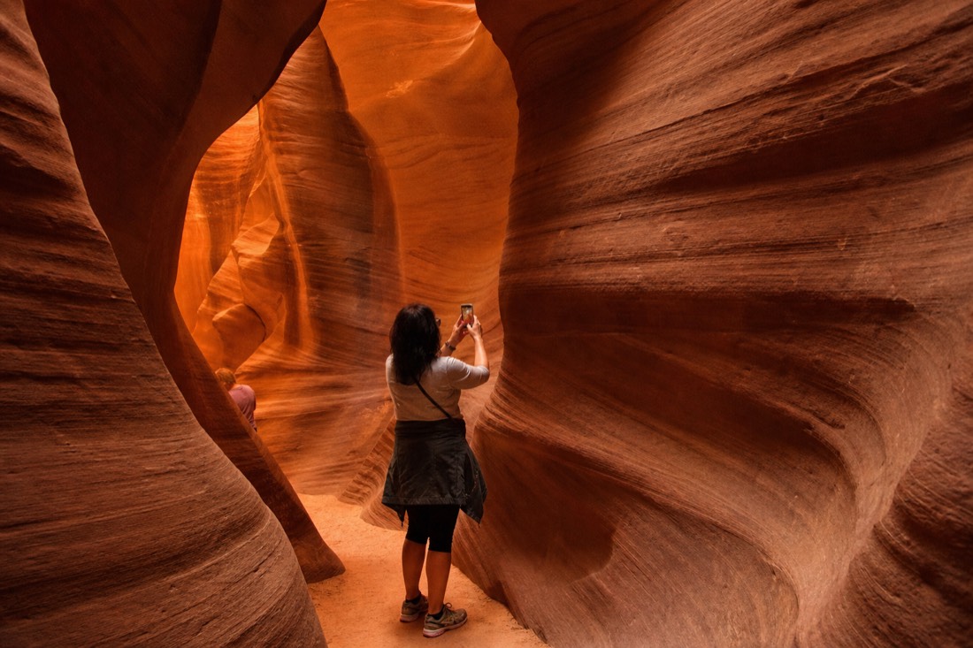 Visitors pausing for photos inside a narrow glowing slot canyon passage