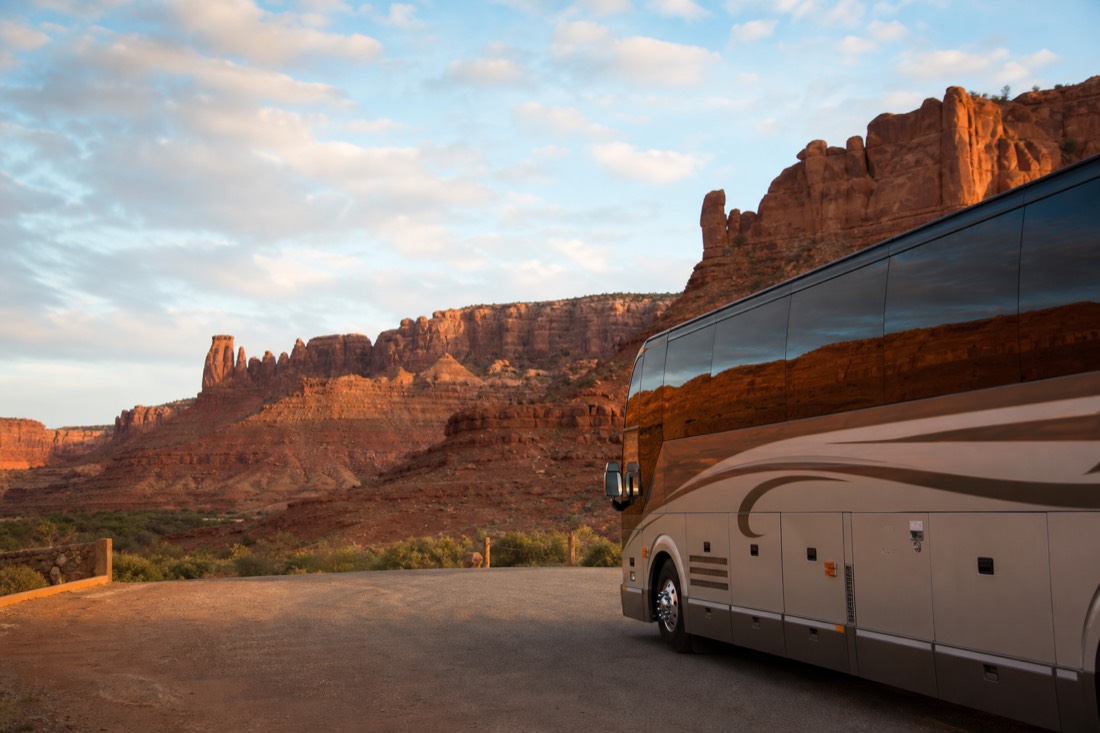 Tour coach parked at a desert overlook while travelers photograph sandstone cliffs