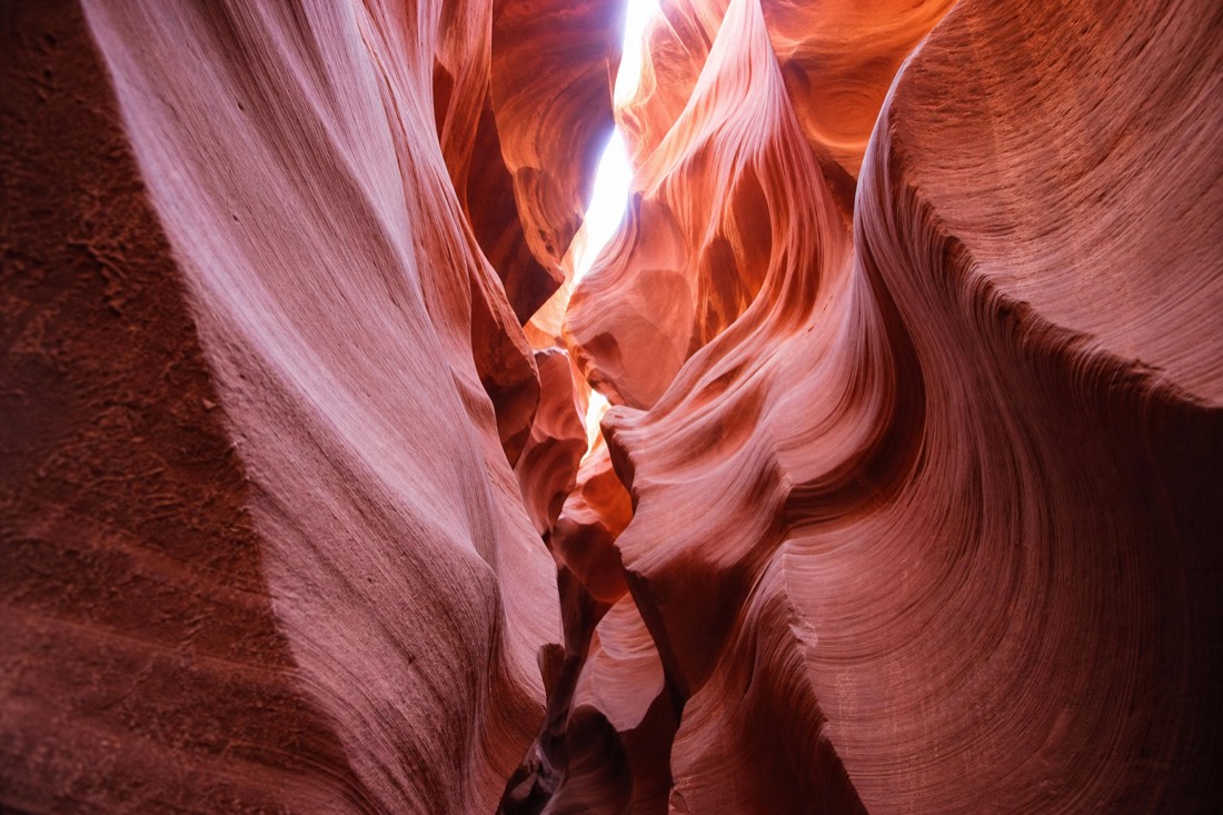 A small guided group walking the tight V-shaped corridor of Lower Antelope Canyon between glowing orange sandstone walls